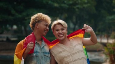 Heyecanlı genç eşcinsel çift şehir parkında duran gökkuşağı bayrağını göndere çekiyor. Neşeli Asyalı erkekler yerel LGBT topluluğunu gururlu ayı kutluyor. Homoseksüel evliliklerin yasallaştırılması