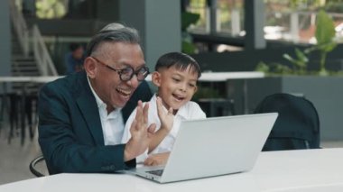 Mutlu Asyalı baba ve oğul, laptoptaki görüntülü sohbeti yavaş çekimde kullanır. Dikkatli Koreli ebeveyn ve küçük çocuk bilgisayar aracılığıyla konferansa katılıyor. Aile yaşam tarzı
