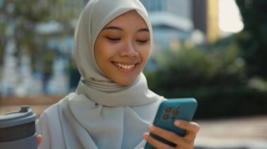 Hijab Walks 'ta güzel bir kız caddeye çıkıyor ve telefonunu kullanıyor, ekranda gülümsüyor. Genç, tatlı Müslüman kadın dışarıda yürüyor ve internetten akıllı telefonuyla video izliyor. İnsanlar, Teknoloji