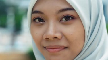 Caddedeki tesettürlü zarif kadın kamerayla göz teması kuruyor. Göz kamaştırıcı genç kız dışarıda duruyor ve yüzü kameraya dönük poz veriyor. Makyaj. Müslümanlar. Yakın çekim. İnsanlar Konsepti