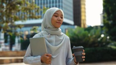 İslami Genç Kadın Bilgisayarla ve Kahve İçerek Ofisten Eve Gidiyor. Kahve molasında dizüstü bilgisayar taşıyan, tesettürlü güzel bayan. Halk ve Teknoloji Konsepti