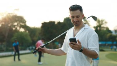 Golf sopalı sakallı adamın portresi spor sahasında cep telefonu ekranına bakıyor. Erkek oyuncu, sosyal medyada yarışmayı kazananlar hakkında haberler okuyor. İnternette pozitif golfçü bahisleri