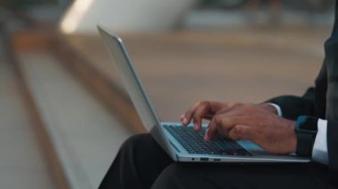 Taşınabilir bilgisayarla çalışan ve merdivenlerde otururken klavyede yazan tanınamayan biri. E- postalar için metin yazarken modern aygıtın düğmelerine basan dijital işçinin elleri.