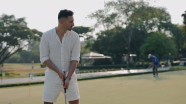 Sürücüsü rotada vurmaya hazırlanan konsantre bir adam golfçü. Beyazlar içindeki odaklanmış erkek golfçü yarışmaya hazır. Banliyö kulübünde yetenekli bir sporcu.