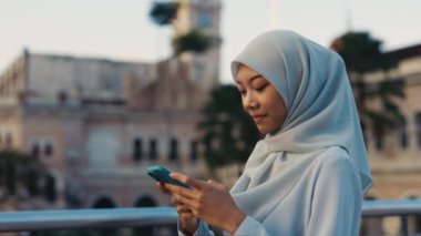 Dışarıdaki Müslüman Kadın 'ın Smartphone kullanarak internette gezinirken görüntüsü. Başörtüsü takan, sohbet eden, çevrimiçi sorunları çözen bir kadın. Halk ve Teknoloji Konsepti