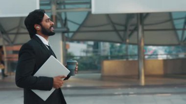 Dijital cihazlar taşıyan klas bir adamın yan görüntüsü ve telsiz kulaklıklardan radyo dinlerken tekrar kullanılabilir bardak. Motivasyonlu şirket yöneticisi şehir şehir ofis binasına doğru ilerliyor..