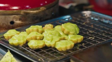 Kanom krok bai toei kekleri serinlemek için ızgaranın üzerine serinlerken yemek maşasıyla bilinmeyen bir insan tarafından seçiliyorlar. Pandan krepleri pazar müşterilerine atıştırmalık olarak servis edilmeye hazırlanıyor..
