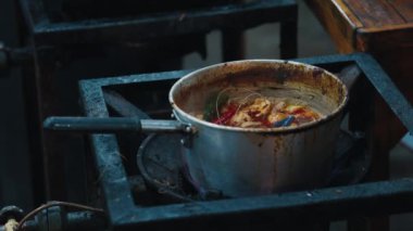 İçinde karides ve baharatlı acılı çorba kaynayan Tayland bitkisi olan kirli bir tencere Tom yum yapışkanı. Geleneksel Asya mutfağı akşam marketinde açık mutfakta pişiriliyor..