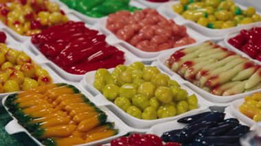 Kanom, geleneksel ışık pazarının vitrininde açık beyaz kaselerde sergilenen şekerlere bak. İsimsiz biri küçük metal cımbızla renkli çeşitlilikten şeker topluyor..