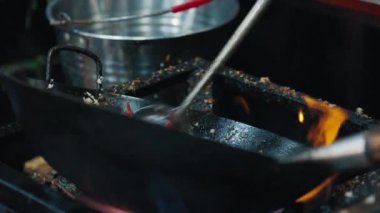 Kirli kenarları olan gaz sobasının üzerinde kimliği belirsiz birinin elinde öğütülmüş et olan demir wog tavası. Gece pazarı çalışanı baharatlı Tayland yemeği hazırlıyor. Baharatlı tavuk salatası, larb gai..