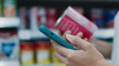 Telefondaki malzemeleri okurken kadın tenekesini tutan narin eller. Genç bayan beslenme bilgilerini takip etmek için akıllı telefonunda Calorie Hesap Makinesi Uygulaması kullanıyor. Alışveriş Konsepti