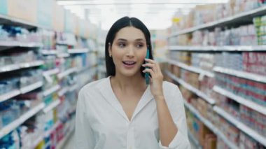 Mağazada gezen, arkadaşlarıyla cep telefonuyla konuşurken ürünlere bakan tatlı, pozitif bir kız. Çekici Kadın Ürün Dükkanına Gidiyor ve Akıllı Telefonla Konuşuyor