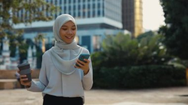 Şirin İslami Kadın Sokakta, Smartphone Holding Coffee 'de mesaj atıyor. Yürüyüş ve sohbet için cep telefonunu kullanan tesettürlü çekici bir kadın. Halk ve Teknoloji Konsepti