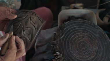 Yaşlanmış birinin kollarını kapatırken, bitmemiş kupanın yumuşak malzemelerine doğal bir şekil oymak için özel bir alet kullanır. Keskin fırça atölyedeki çiğ seramik öğede geleneksel desen oluşturuyor.