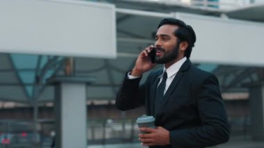 Beyaz gömlekli, siyah ceketli, kenar mahallede gezen telefon ve kahve fincanı ile konuşan keyifli bir adamın yan görüntüsü. Olumlu iş adamı, iletişim
