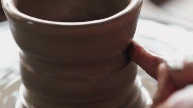 Tanımlanamayan çömlek ustasını parmaklarıyla dönen yüzeye yerleştirilmiş ıslak kil nesneleri iterek kapatın. El sanatları stüdyosundaki yeryüzü donanımı tasarımı ve şekli üzerinde çalışan konsantre bir insan..