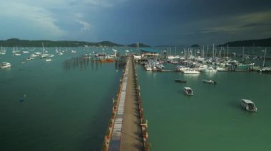 Adam Phuket Tayland 'da uzun iskele boyunca motosiklet sürüyor. Modern yat kulüpleri turkuaz sularda turistler için güneşli bir günde doğayı keşfetmek için eğlenceli deniz maceraları sunuyor.