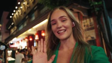 Gece Sokağında sosyal medya için kameraya bakan pozitif kadın blog yazarı POV 'u. Mutlu kadın, akşam megapolis 'te seyahat blogu için lüks alışveriş merkezinin tanıtımını gösteriyor.