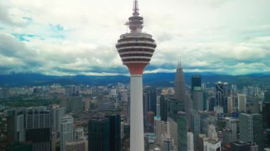Menara Kuala Lumpur Kulesi, modern gökdelenlerle çevrili şehir silueti üzerinde yükseliyor ve bulutlarla dolu dramatik bir gökyüzü, şehir hayatının özünü yakalıyor..