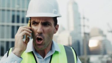 Sert şapkalı bir mühendisin portresi telefonda öfkeyle konuşuyor ve başka tarafa bakıyor. Yelekli erkek müteahhit inşaat alanında teknik arızalarla karşılaşan işçilere bağırıyor