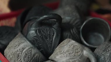 Büyük miktarda açık ve koyu gri fincanlar, küçük detaylarla süslenmiş ve sepetin içinde yığılmış vaziyette duruyor. Doğulu usta tarafından sokak pazarında satışa hazır kırsal mutfak malzemeleri üretildi..