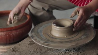 Yüzsüz insan, terracotta kasesinden palmiye ile kirli su alıyor ve fırlatma tekerleğine sıvı katıyor. Çizgili önlük konusunda deneyimli profesyonel. Modellik için malzemeyi kolaylaştırıyor..