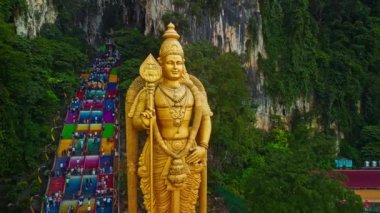 Lord Murugan 'ın Malezya' daki Batu Mağaraları 'ndaki görkemli altın heykeli. Bölgeyi saran renkli basamaklar ve yemyeşil alanlar.