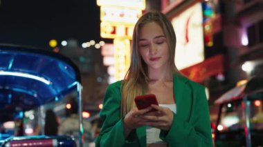 Canlı kıyafetli mutlu sarışın bir kadının portresi. Gece telefonuna mesaj yazıyor. Olumlu ifadeli güzel bir kadın. Akşamları akıllı telefondan internette sohbet ediyor.