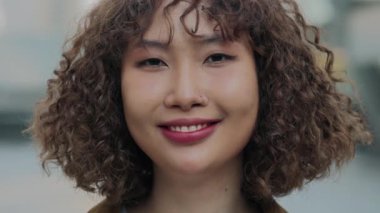 Kıvırcık saçlı genç bir Asyalı kızın Kıvırcık portresi. Dışarıda dururken mutlu bir şekilde gülümsüyor. Lady Outdoor, Neşeli Surat 'la kameraya bakıyor. İnsan ve Gençlik Konsepti