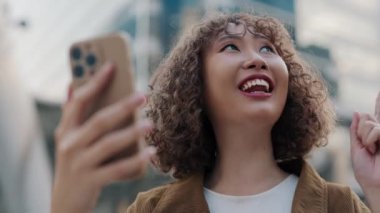 Asyalı Kadın dışarıda şık giyinmiş bir şekilde dikilirken arkadaşlarıyla video görüşmesinde heyecanlı hikâyeler anlatıyor. Çekici Olumlu Kadın İş Konferansı 'ndan bildiriyor. Halk ve Teknoloji