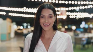 Genç, kendinden emin, uzun saçlı, beyaz gömlekli, dışarıda duran güzel bir kadının portresi. Gece Kafesi 'nin çekici sahibi kameraya bakıyor ve gülümseyerek poz veriyor. İnsanlar Konsepti
