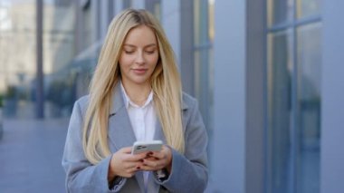 Çekici Sarışın Profesyonel Yürüyüş Kadını ve Şirket Binası dışında cep telefonuyla mesajlaşma ile meşgul. İş kadını, akıllı telefonunu kullanıyordu. İş ve Teknoloji Konsepti