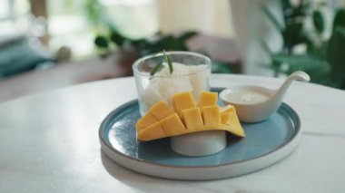 Hindistancevizi sosu ve yeşil bir tabakta dinlenen taze mango dilimleriyle birlikte bir bardakta sunulan lezzetli bir mango pilavı..