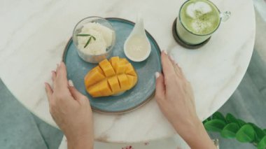 Mangoyu seven bir kadın hindistancevizi kremalı pilav ve tropikal bir kafede Matcha Latte içiyor. Yakın çekim. Üst Görünüm