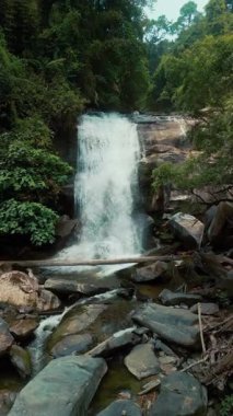 Yoğun yeşil bir ormanda kayalık arazide akan sakin bir şelale. Doğa ve sükunet kavramı. Çevre turizmi ve açık hava keşfi için manzaralı bir yer. Hava Görünümü, dikey çekim