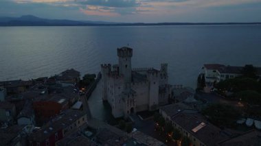 Alacakaranlıkta Sirmione, İtalya 'daki Scaliger Kalesi' nin insansız hava aracı çekimi. Garda Gölü ile çevrili ortaçağ kalesinde tarihi mimari ve manzaralı kıyı manzaralar sergileniyor..
