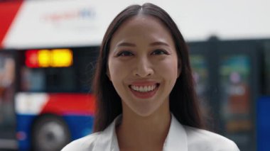 Gülümseyen genç bir iş kadınının portresi. Resmi giyinmiş otobüs durağının dışında duruyor. Dışarıdaki muhteşem Asyalı kadın parlak bir gülümsemeyle kameraya bakıyor. İnsanlar Konsepti