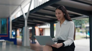 Muhteşem Neşeli İş Kadını otobüs durağının yanında oturuyor ve online konferansta dizüstü bilgisayarla müşterileri selamlıyor. Videodaki genç kız bilgisayarla arıyor. Halk ve Teknoloji Konsepti.