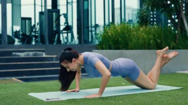 Spor hocası modern spor salonunda dizlerinin üstünde şınav çeker. Esmer kadın, mobil uygulamayla vücut kaslarını çalıştırıyor. Eşofmanlı bayan antrenmanda güç ve dayanıklılık uygular.