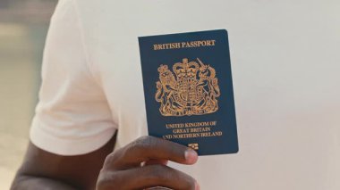 Günlük kıyafetli Afro-Amerikan bir adam İngiliz pasaportunu elinde tutuyor. Adam gururla vatandaşlık statüsünü kabul ediyor. Erkek, başarılı göçü kutluyor