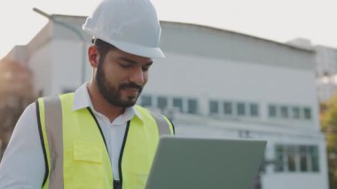 Bilgisayarda endüstriyel binalara karşı çalışan pozitif ırk teknisyeninin portresi. Sakallı olgun mühendis inşaat alanını kontrol etmek için dijital cihaz kullanıyor. Boşluğu kopyala