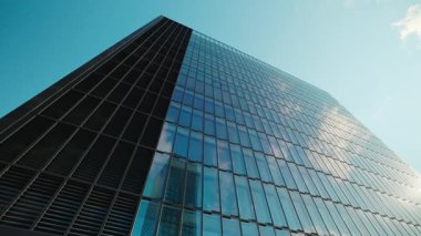 Ofis cephesi panoramik pencerelerle kaplı şehir merkezindeki bulutları ve açık gökyüzünü yansıtıyor. Kentsel çevredeki şirket genel merkezi. Mimari eğilimler