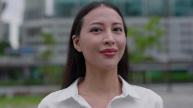 Güzel Gülümseyen, Dışarda Duran ve Kameraya Bakan Pozitif Kız. Açık havada gülümseyen Asyalı genç iş kadınının portresi. İnsanlar Konsepti