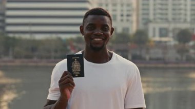 Kameraya bakarak Kanada pasaportunu gülümseyen bir adamın portresi. Afrikalı Amerikalı adam şehir seti üzerindeki küresel çalışma programına kabul edilmesini kutladı