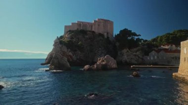 Tarihi Lovrijenac Kalesi, sakin deniz limanı kameraları üzerinde yüksek uçurumlarda ilerliyor. Dubrovnik şehrinin eski tahkimatları temiz gökyüzü manzarasına karşı. Doğa görünümü