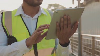 Yelekteki taskmaster tablet bilgisayarına veri yüklüyor inşaat alanındaki işlemleri kontrol ediyor. Becerikli mühendis elleri altyapı geliştirme aygıtını tutuyor