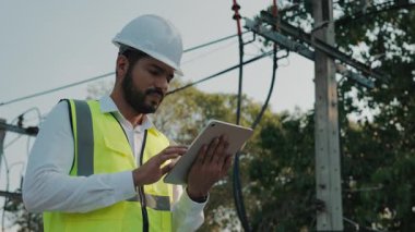 Park yerinde tablet tutan elektrik iletim hatlarını izleyen güvenlik müfettişinin portresi. Koruyucu iş giyimi konusunda deneyimli mühendis inşaat alanındaki elektrik ağını kontrol ediyor