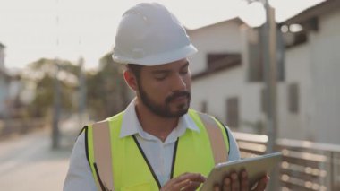 Tabletle yeni binaları ve kamu hizmetlerini izleyen olgun teknisyenlerin portresi. Yoğunlaştırılmış mühendis, şehir ortamında taşınabilir bilgisayar kullanarak inşaat alanını inceliyor