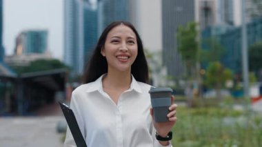 Gülümseyen kadın işten sonra elinde evraklar ve bir fincan kahveyle sokakta yürüyor. Pozitif ofis çalışanı, kahve molası sırasında çalışma evraklarını taşır ve şehri gezer..