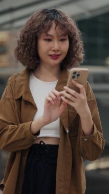 Dikey video. Smartphone 'daki zaferini sokakta şık kıyafetler giyerek kutlayan mutlu kız. Heyecanlı Genç Bayan Para ve İş Hakkında Akıllı Telefonundan Olumlu Haberler Alıyor